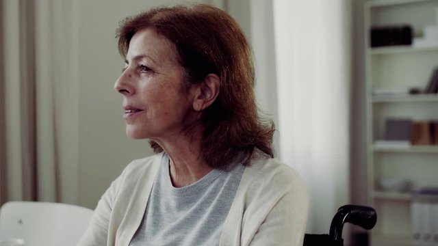 Senior woman in wheechair sitting at the table at home, talking to somebody.