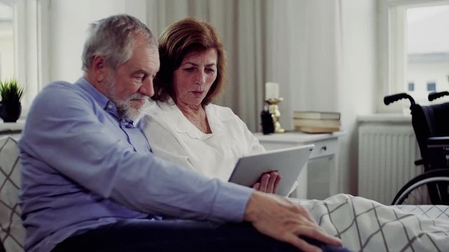 A senior couple with tablet at home, a husband spending time with his ill wife.