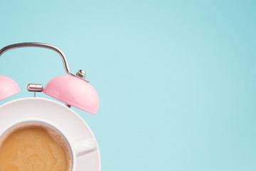 Pink alarm clock and coffee cup on blue background. Breakfast time concept. Minimal style