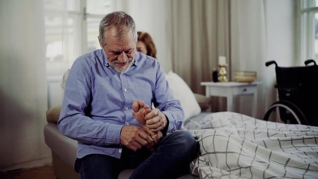 A senior man and his disabled wife sitting on bed, giving a foot massage.