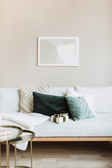 Modern interior design concept. Minimal Nordic Scandinavian style living room with photo frame on pastel beige wall, sofa with pillows and gift box. Comfortable apartment for rent.