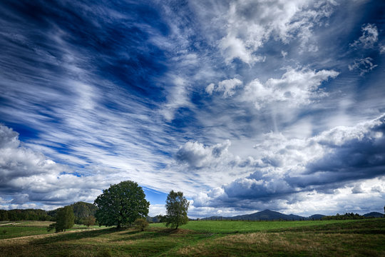 Czech summer landscape. Beautiful white clouds on the blue sky above the green meadow with trees. Wet rainy season. Wild nature,  travelling in Europe.