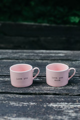 Two pink cups are standing on the wooden table with inscription 