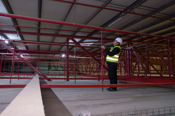 Technician engineer in a whute helmet checks the sprinklers pipes and roof constractions with a...