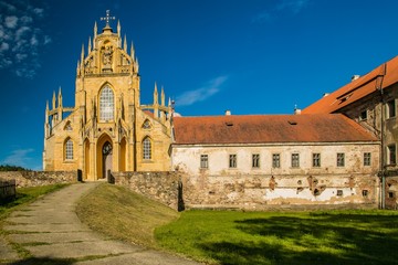 Fototapeta na wymiar Kladruby, Czech Republic / Europe - July 7 2018: Church of the Assumption of the Virgin Mary built in baroque gothic style, historical stone buildings with red roofs, sunny day, blue sky, green grass
