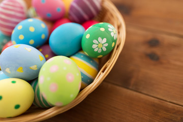 Fototapeta na wymiar easter, holidays and tradition concept - close up of colored eggs in basket on wooden table