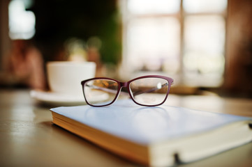 Close up photo of notebook with glasses against cup of coffe at cafe table. Eyewear concept.