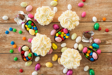 easter, food and holidays concept - frosted cupcakes with chocolate eggs and candies on wooden table