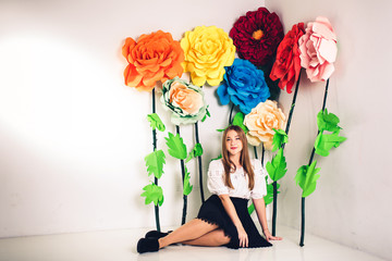 funny young girl sitting on the floor in the studio on the background of large artificial flowers.