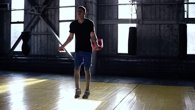Front view of man in blue shorts skipping rope in a boxing gym. Cardio workout and boxing. Concept of a healthy lifestyle. Jumping high with rope
