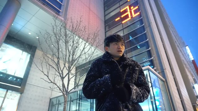 Young Asian Man is Cold and Rubs Hands Together in Attempt to Stay Warm During Cold Sub-Zero Freezing Winter Weather in City