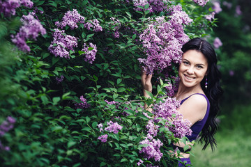 attractive woman in purple dress posing near lilac flowering bushes