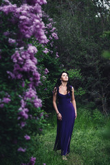attractive woman in purple dress posing near lilac flowering bushes
