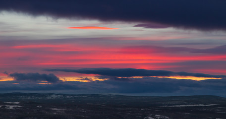 Panorama of a sunset in Idre, Sweden with a pink circular cloud in the vibrant sky, photographed in winter. 