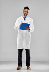 medicine, science and profession concept - smiling indian male doctor or scientist in white coat with clipboard over grey background