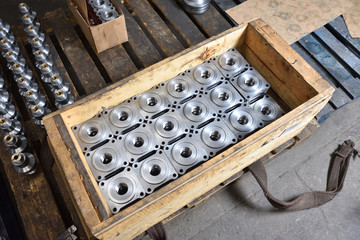 Metal square parts for valves of water or gas, lie in a wooden box at the factory