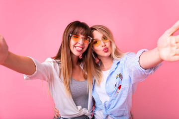 Photo of two young party women smiling and waving hand at camera while taking selfie photo on...