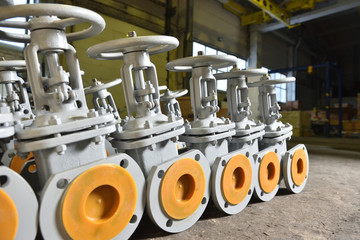 Several new gray valves, for water or gas, lie on the floor at the factory. The valves are gray for...