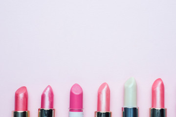 Set of colored pink lipsticks on pink background. Women's cosmetics. Selective focus. Copy space.