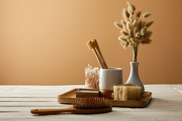 wooden tray with different hygiene and care items, vase of spikelets, and hair brush on white...