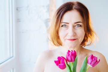 Life is beautiful spring tenderness concept Studio close up portrait of a beautiful mid aged european woman with pink tulip flowers smiling copy space.