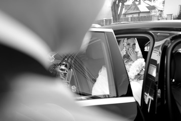 Groom open the door of wedding car and take hand to bride and smiling.