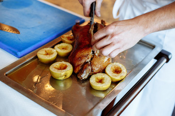 cook cuts roast duck, apples on baking sheet
