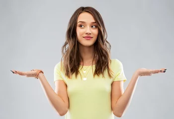Fotobehang choice and people concept - smiling young woman or teenage girl in blank yellow t-shirt holding something imaginary over grey background © Syda Productions