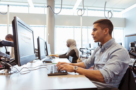 Serious male and female students using computers at desk in university library
