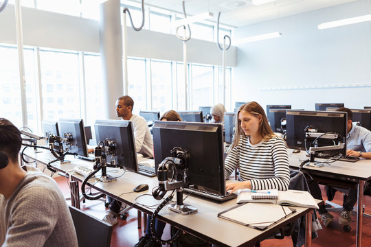 Male and female young students using computers at desk in university library