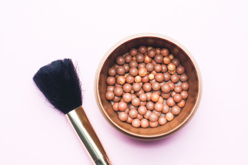Blush balls in the jar and brush cosmetic on a pink background.