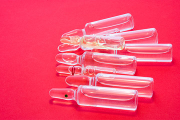 Many pharmaceutical transparent vials with medicine lie on red background. Concept photo of cycle of injection patient treatment, pharmaceutical industry or factory production.