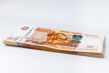 Marriage rings on а stack of many banknotes of five thousand Russian rubles on a white background