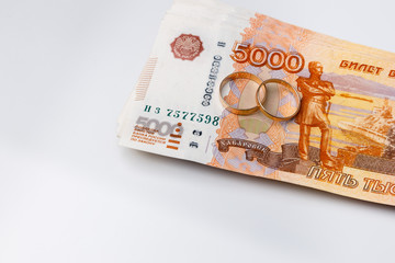 Marriage rings on а stack of many banknotes of five thousand Russian rubles on a white background