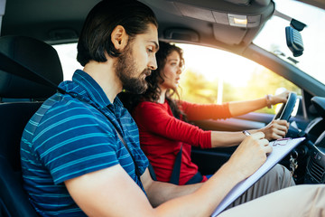 Driving school or test. Beautiful young woman learning how to drive car together with her instructor.