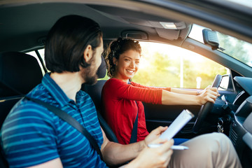 Driving school or test. Beautiful young woman learning how to drive car together with her...