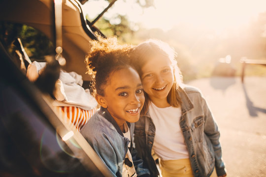 Portrait of smiling friends sitting in car trunk