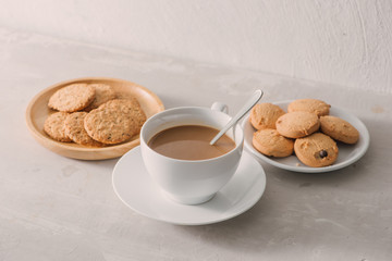 Cup of coffee with milk or cappuccino with cookies on light stone background. Drink with caffeine or cocoa with milk. Coffee break concept.
