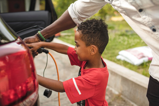 Father and son connecting cable to electric car on driveway
