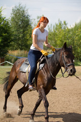 A redhead woman riding a horse on a farm