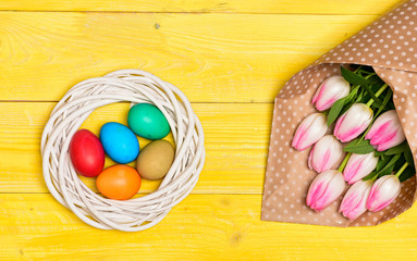 Tradition celebrate easter. Happy easter season. Easter eggs symbol. Spring vibes. Easter is coming. Colorful bright eggs and bouquet fresh tulip flowers on yellow background top view. Spring holiday