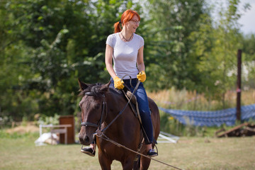 A redhead smiling woman riding a horse on the field.