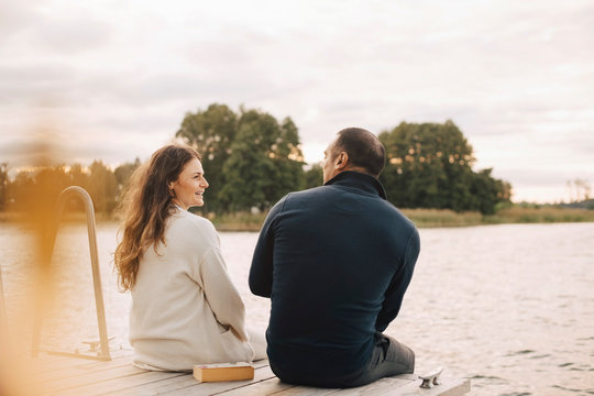 Smiling couple sitting on dock by lake