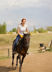 A redhead woman in yellow gloves riding a horse on the field.