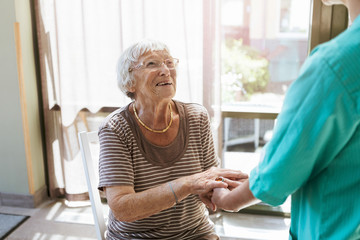Smiling senior woman holding hands of nurse at home
