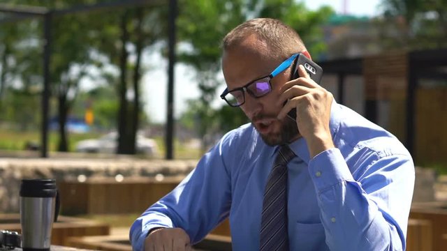 Angry businessman with documents talking on cellphone at city park