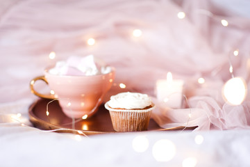 Cute creamy muffin with cup of coffee on tray closeup over light. Good morning.