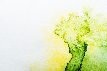 top view of yellow and green watercolor spills on white paper
