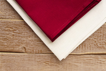 close up of cloth napkins of beige, and burgundy colors on rustic brown wooden table.