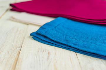 close up of cloth napkins of beige, blue and burgundy colors on rustic white wooden table. Shallow depth of field.